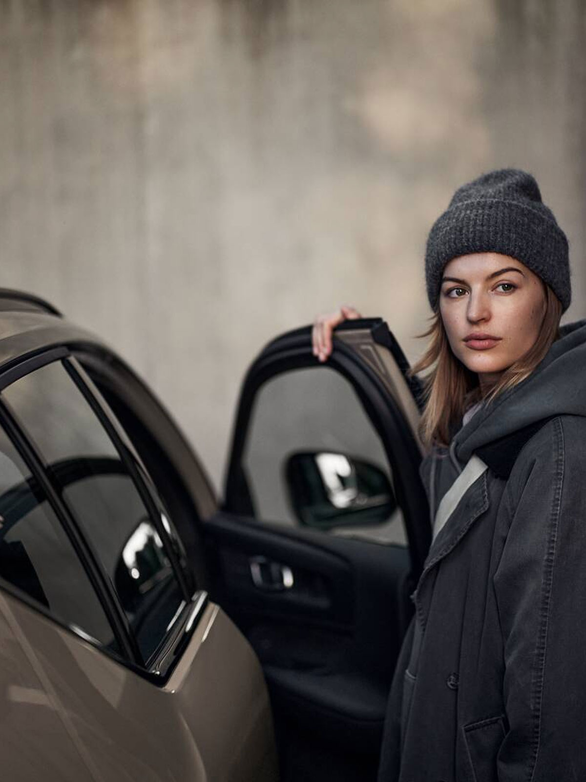 Kvinna med mössa öppnar dörren på en helt elektrisk EX30 i utomhusmiljö.