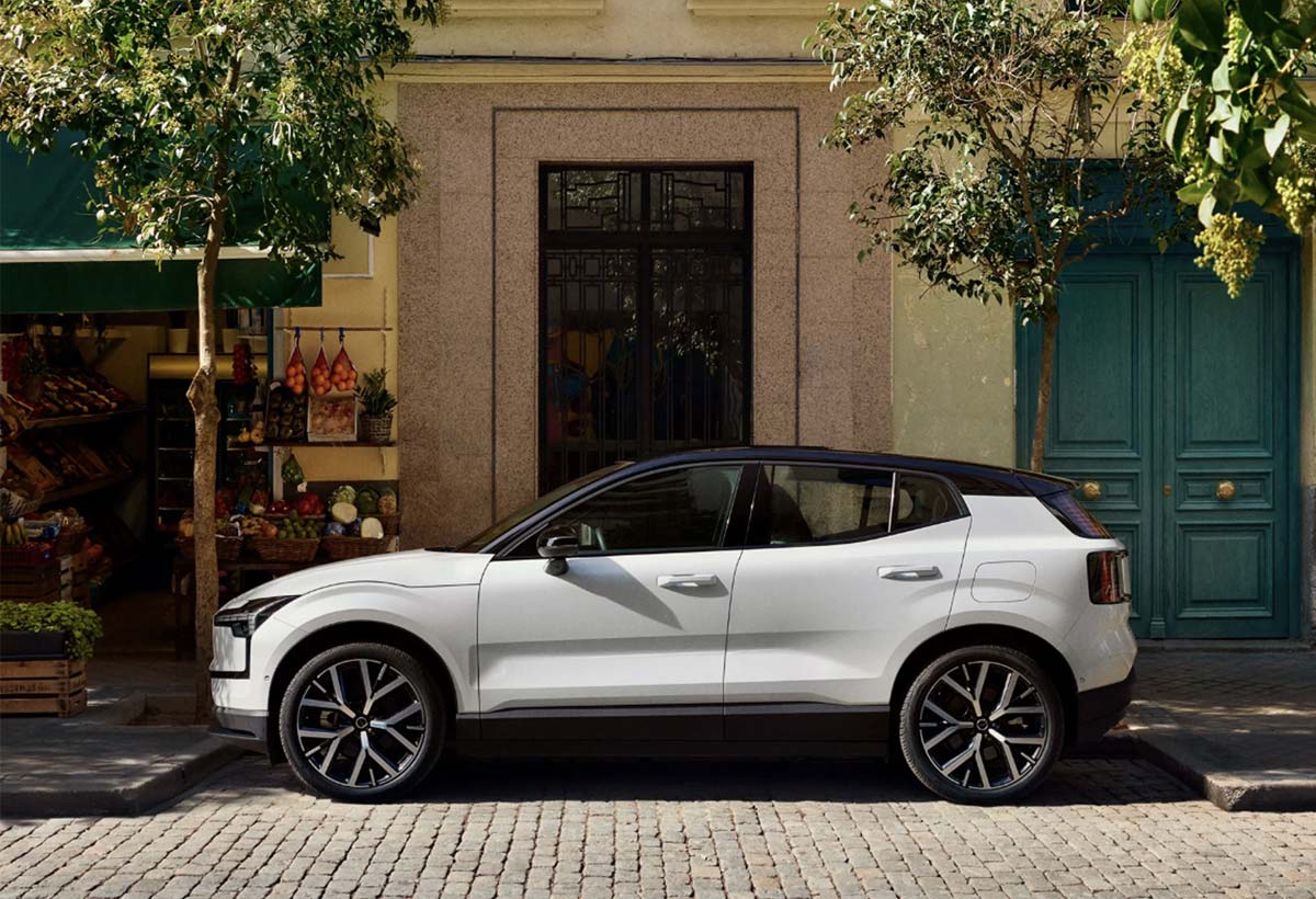 Vit helt elektrisk EX30 sedd från sidan, parkerad i en grönskande stadsmiljö.