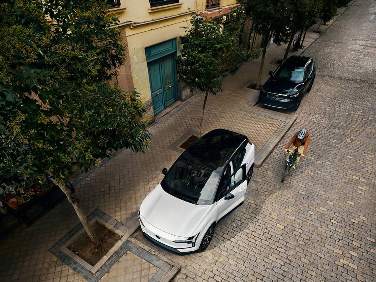 Vit helt elektrisk EX30 parkerad på en kullerstensgata med en cyklist som passerar i stadsmiljö.